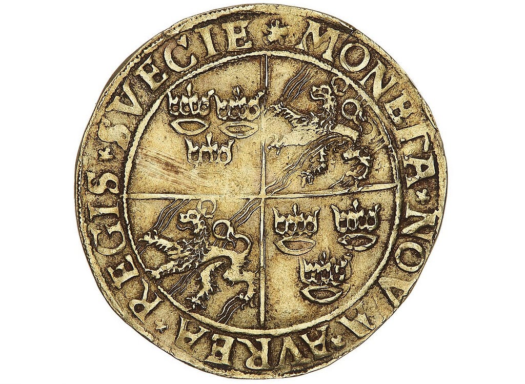 A golden coin with several crowns and two lion figures printed on the coin, as well as text in Swedish.