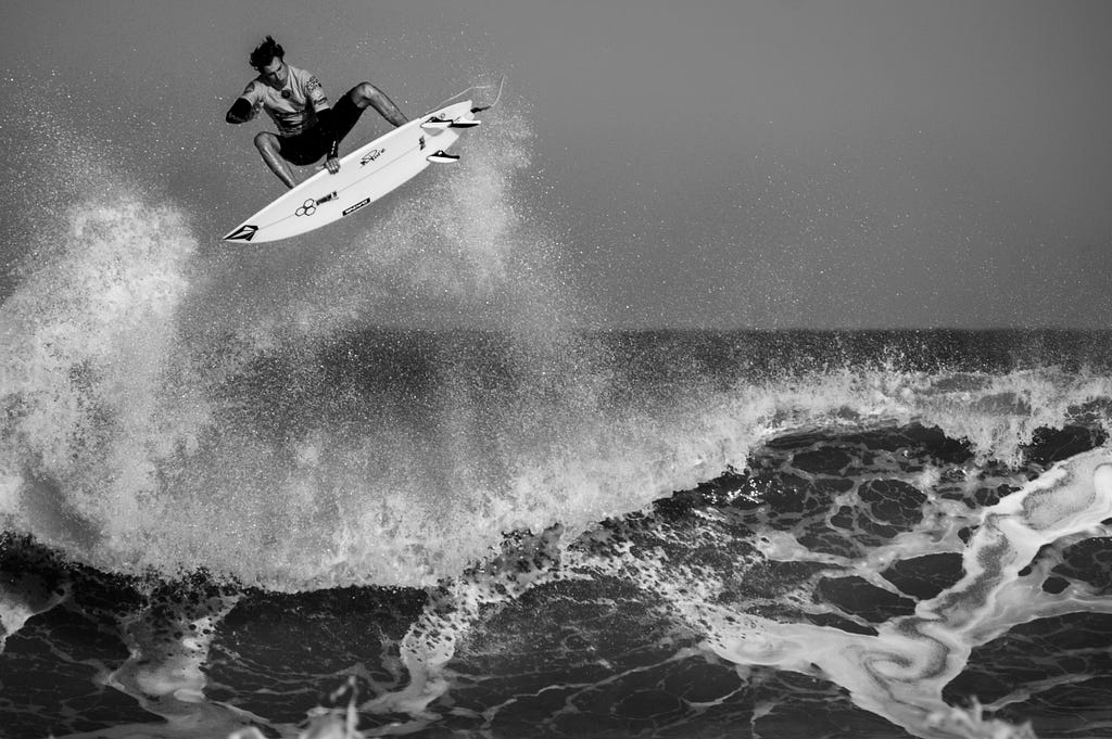 Man riding a wave on a surf board. He’s in the air!