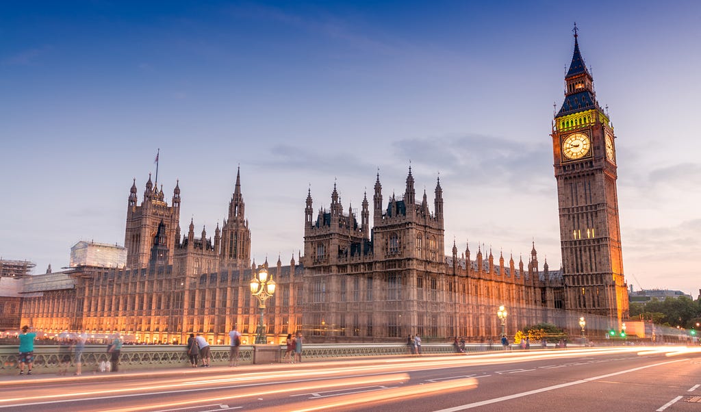 The UK Houses of Parliament at dusk, with Elizabeth Tower (Big Ben) on the right hand side, and light streams from traffic passing over Westminster Bridge in the foreground