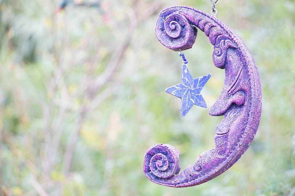 Purple man in the moon decoration with a star hanging down and a background of plants