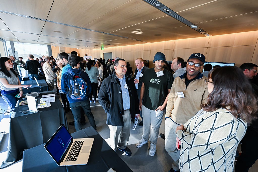 A group of people standing and talking around a table with a laptop.