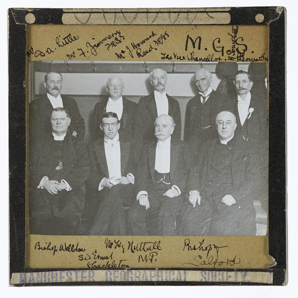 A photographic slide of select members of the Manchester Geographical Society (all male) in Victorian formal dress. They include the Vice Chancellor of the University, a local M.P. and the Bishop of Salford. They are accompanied by explorer Ernest Shackleton.