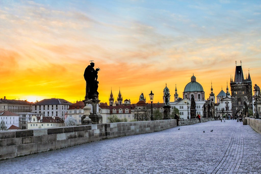 Charles Bridge in Prague with statues, buildings and yellow sunrise