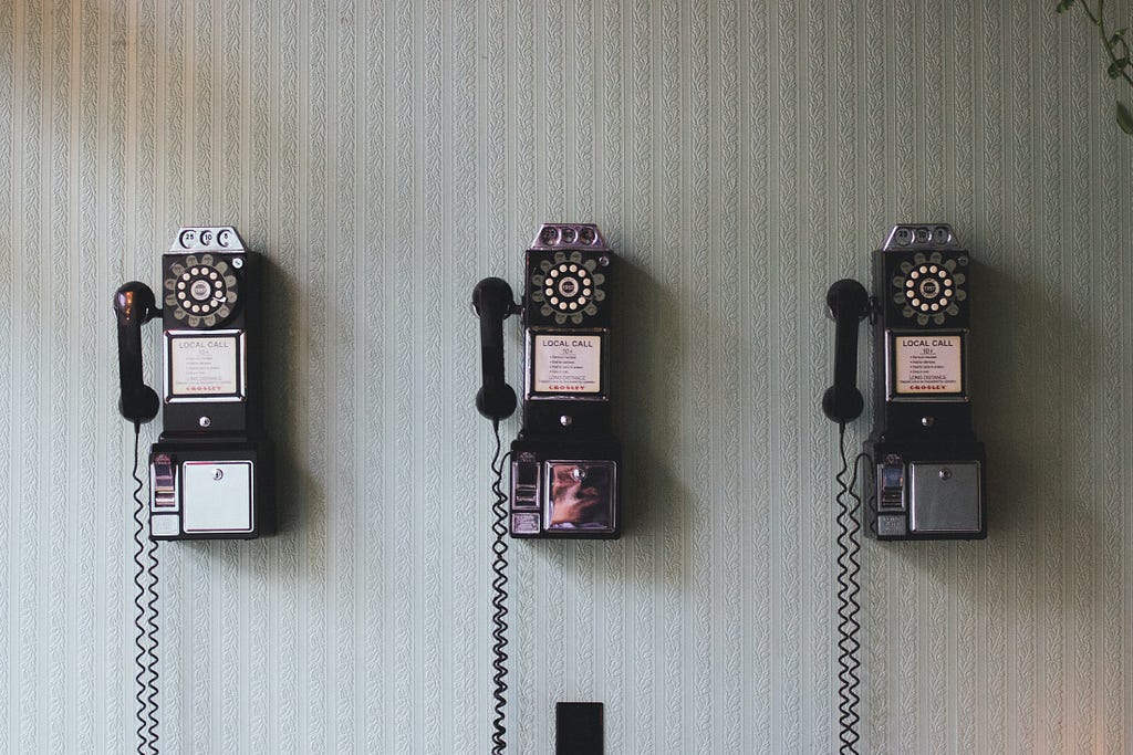3 telefones da década de 70 ou 80 em uma parede com papel de parede listrado