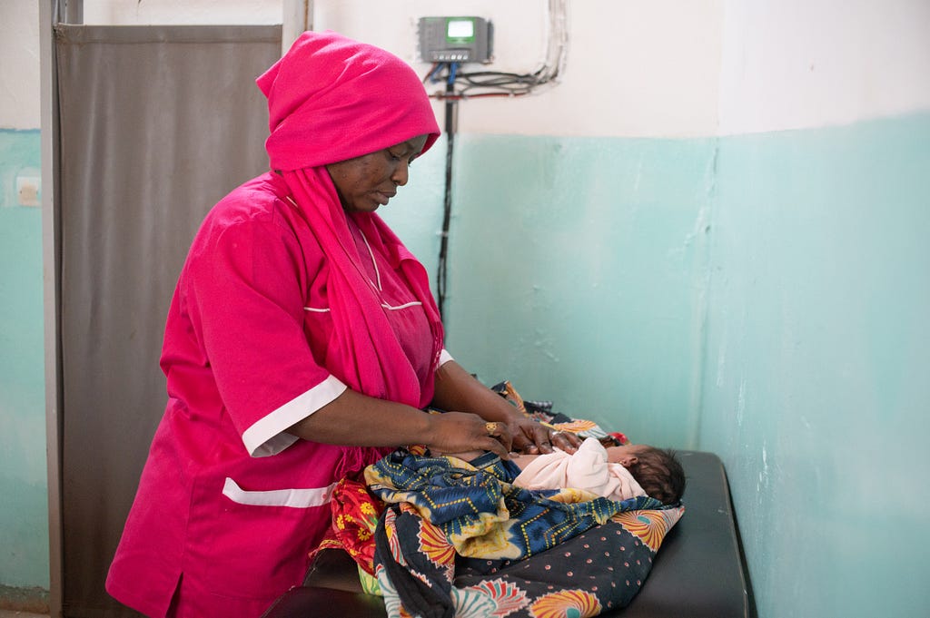 A baby on an examination table is examined by a health worker.