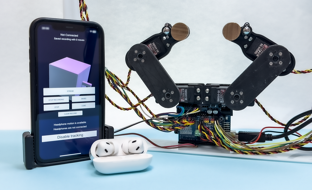 An iPhone and Airpods with the Magnetform robot in the back.