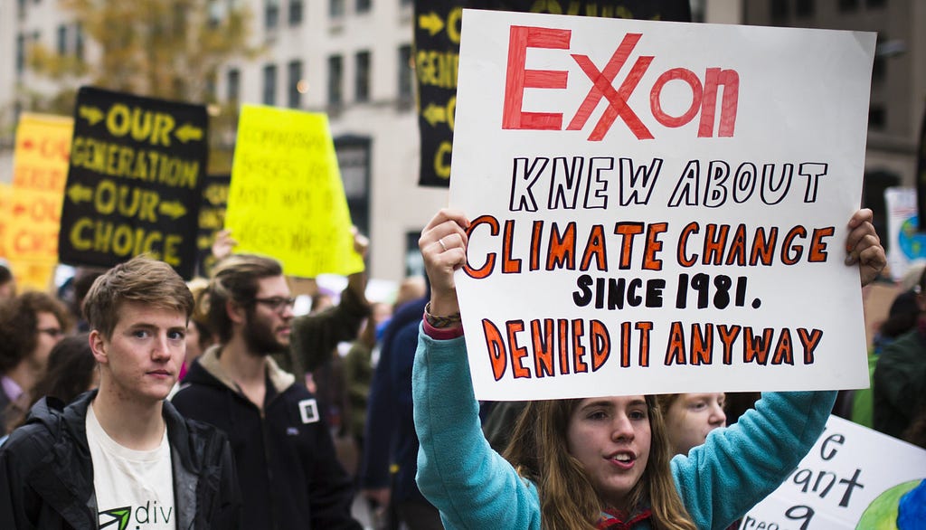 Protester holds sign: Exxon knew about climate change since 1981 and denied it anyway