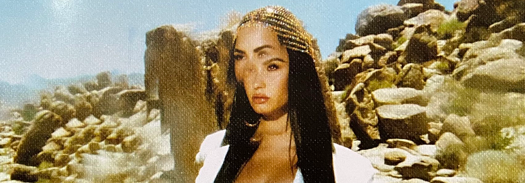 Demi Lovato com cabelos soltos e um enfeite dourado no cabelo. Atrás dela, várias pedras empilhadas