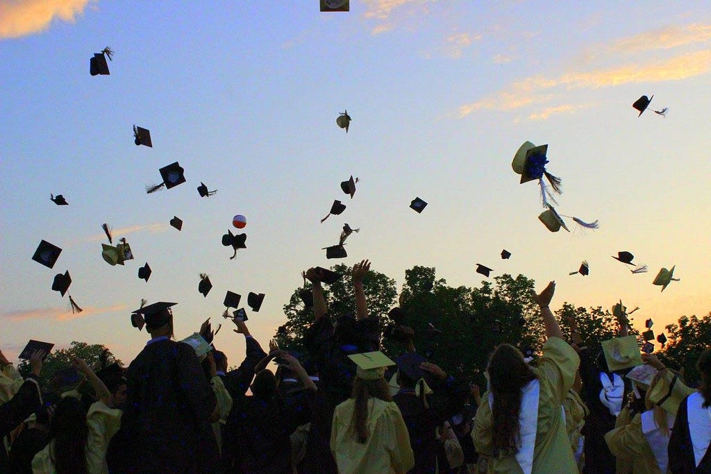 Graduation caps hang in mid-air as high school students who threw them watch from the ground.