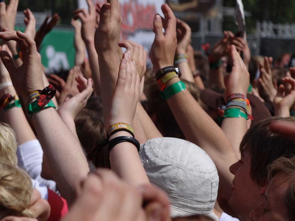 Image of a crowd of people with their hands raised ready to clap. It looks like the crowd is at an outdoor music festival.