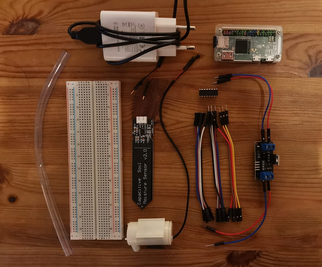 Some requirements placed on a wooden table: modified USB cable as external power source, Raspberry Pi Zero, PVC tube, solderless breadboard, moisture sensor, pump, ADC MCP3008, jumper wires and mosfet relais