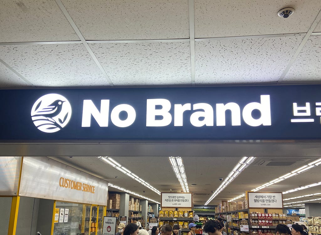 Fachada de uma loja chamada No Brand, escrito em branco sobre uma placa preta. As letras são retroiluminadas e por isso brilham.