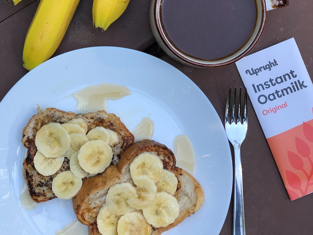 French toast breakfast with bananas, maple syrup, and coffee in a mug with Upright Instant Oatmilk on the side.