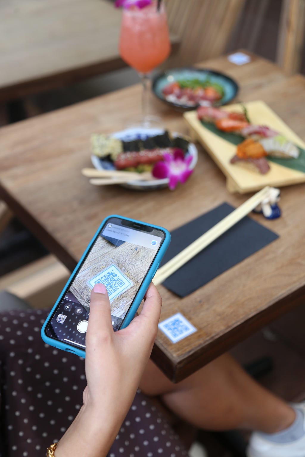 A phone scanning a QR code from a table that is laid with sushi plates.