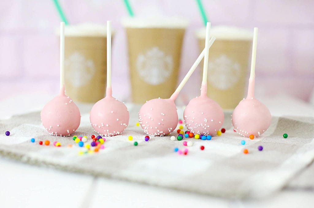 Decorated Starbucks birthday cake pops with colorful sprinkles and ribbon.