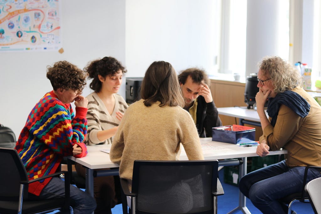 Image of five people around a table in discussion, and writing their thoughts on a large piece of paper on the table