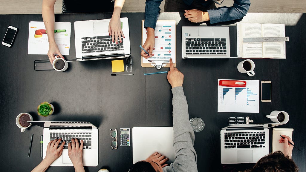 A picture showing office professionals around a desk, at work.