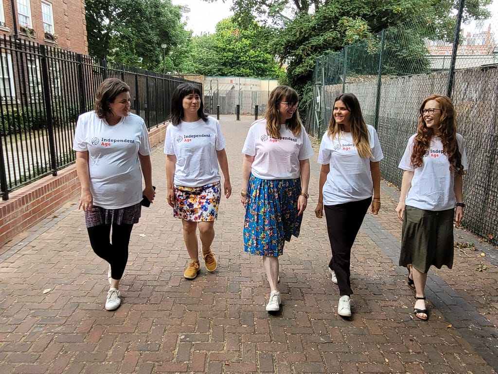 Independent Age staff smile at each other as they walk towards the camera. They are wearing Independent Age t-shirts.