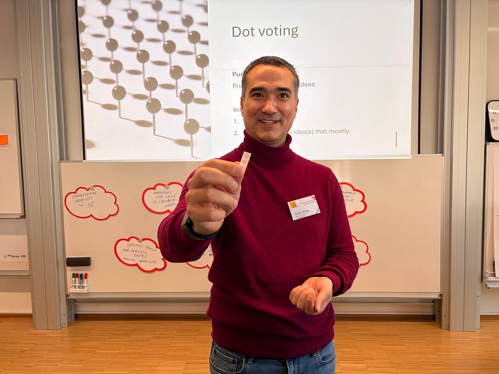 Daniel Russo handing dot stickers to me in front of a slot that says “Dot Voting”.