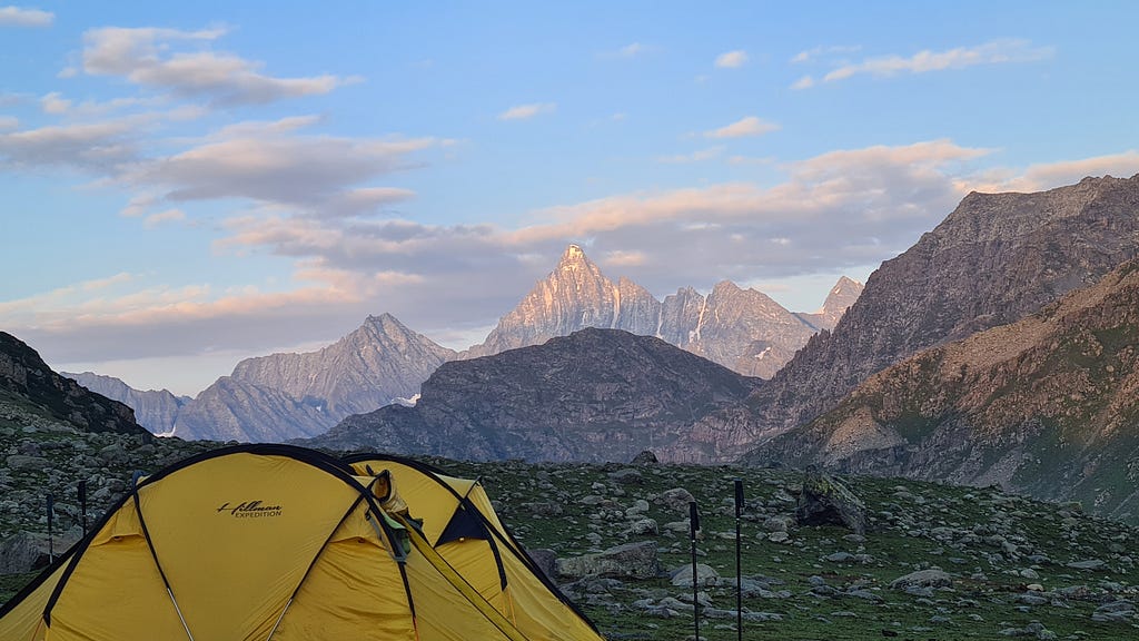 A yellow tent surrounded by majestic mountains.