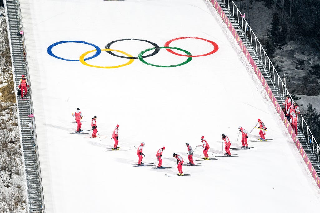 An image of skiers at the Winter Olympics skiing down a ramp with the Olympics rings on it