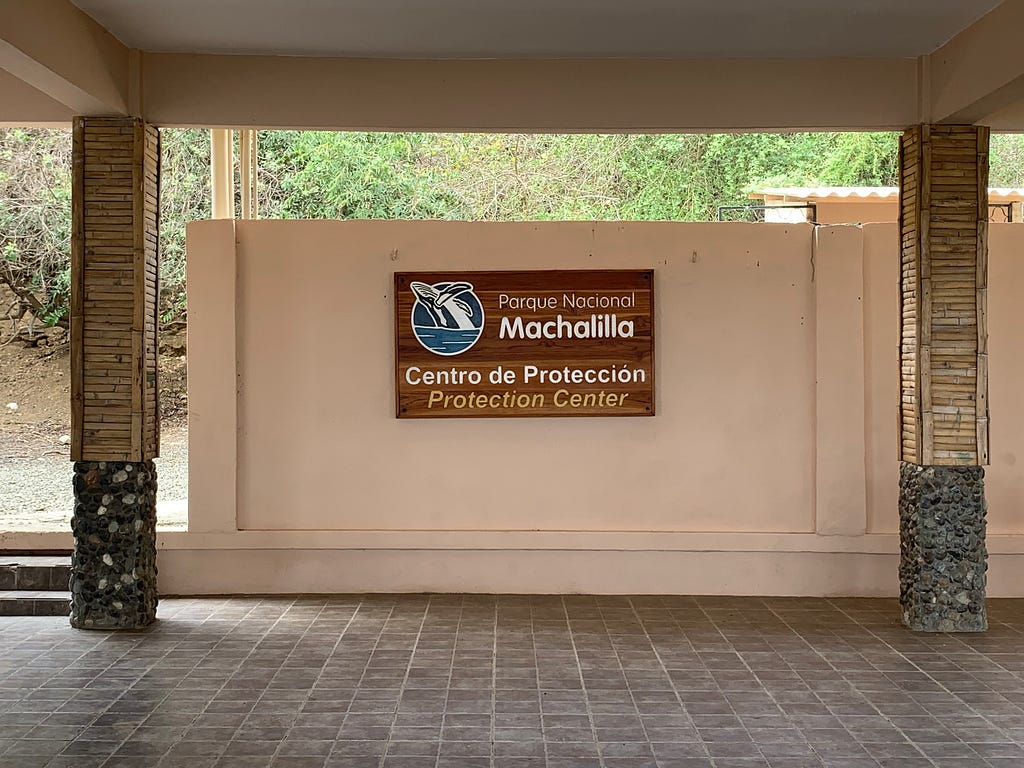 Wooden sign for the Parque Nacional Machalilla, Center of Protection. In the upper left hand corner is a humpback surfacing.