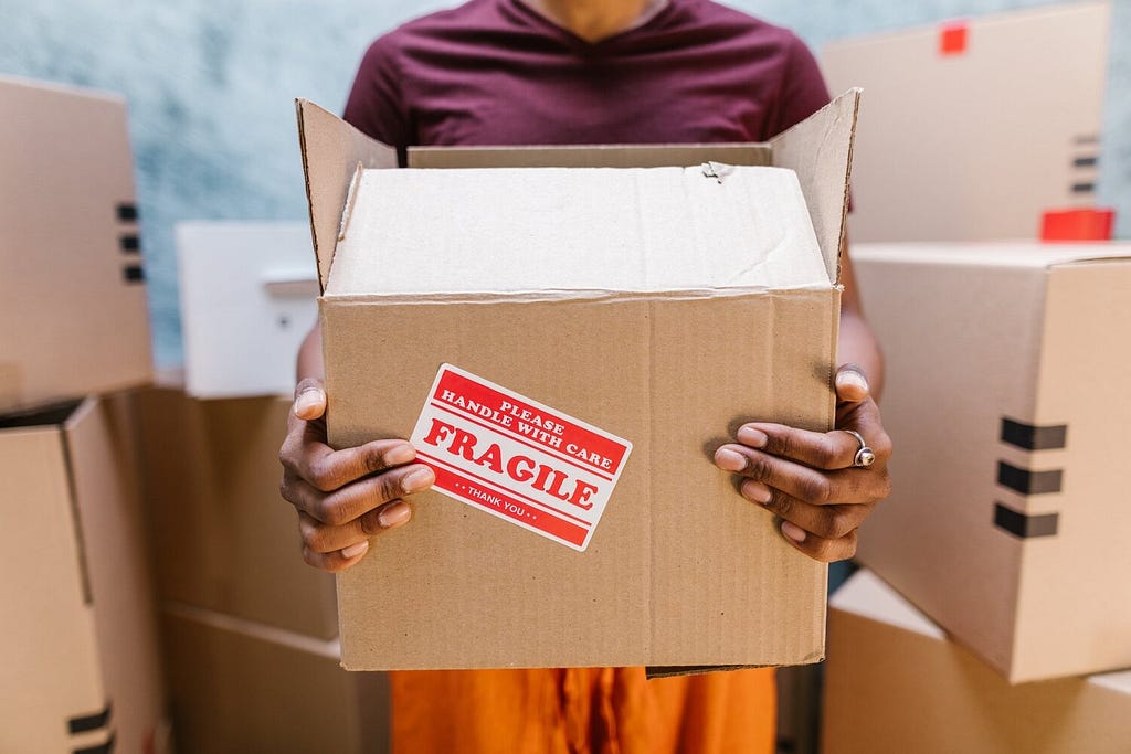 A warehouse employee holds a fragile box with care. Part of white-glove delivery is proper labeling of packaged goods that require special care. Fulfillment means avoiding breaks, spills, tears and malfunctions by handling with care