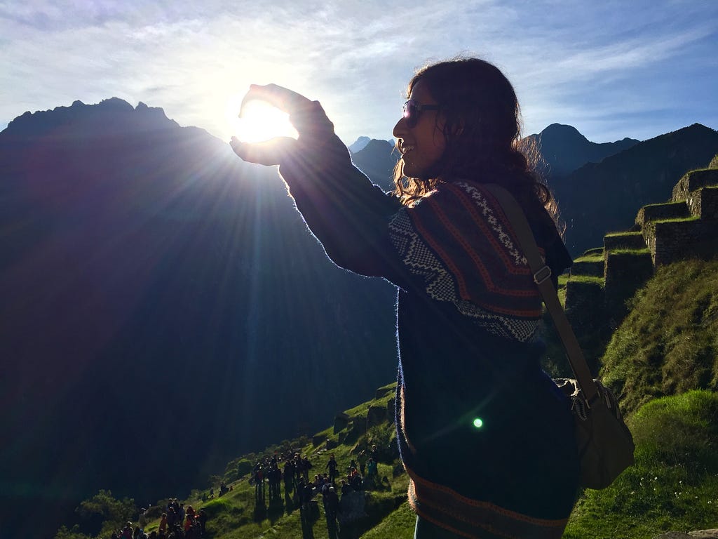 An American female traveler poses for a forced perspective photo during sunrise in Machu Picchu in Peru