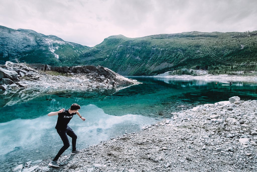 A man throwing a rock into a lake surrounded by mountains