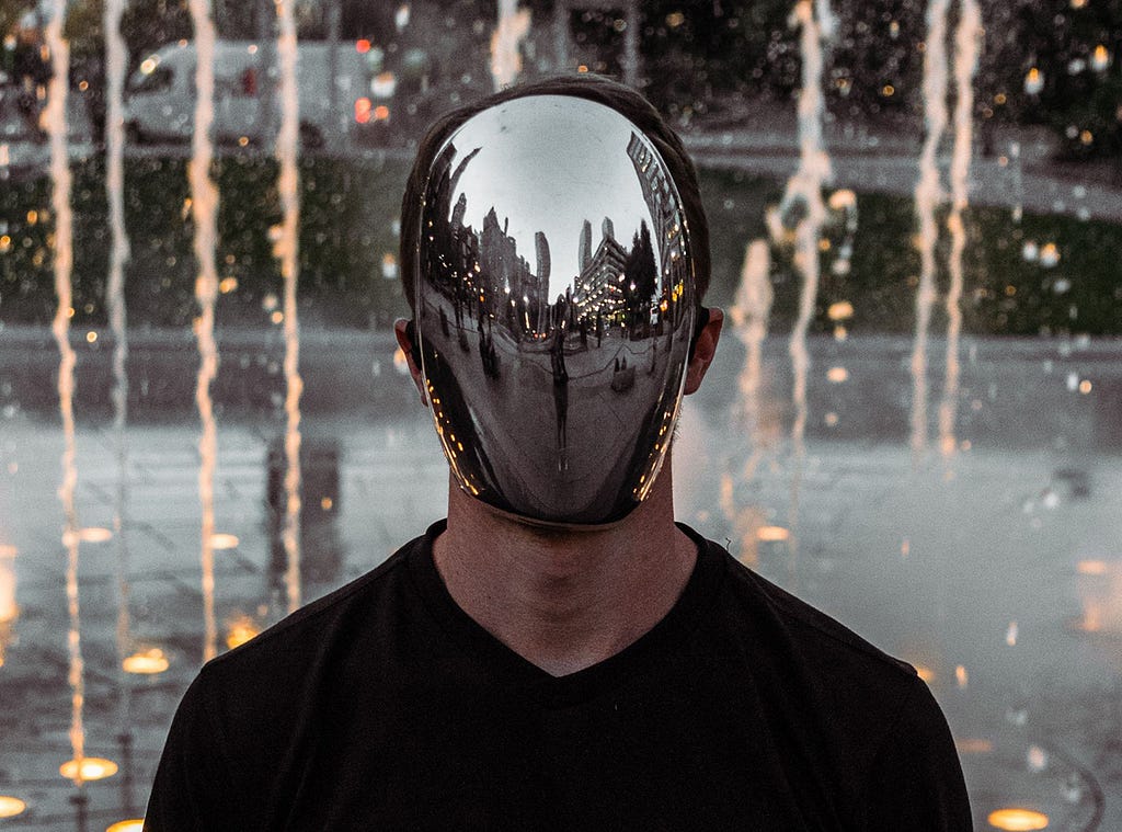 Man with mirrored mask in front of a fountain.