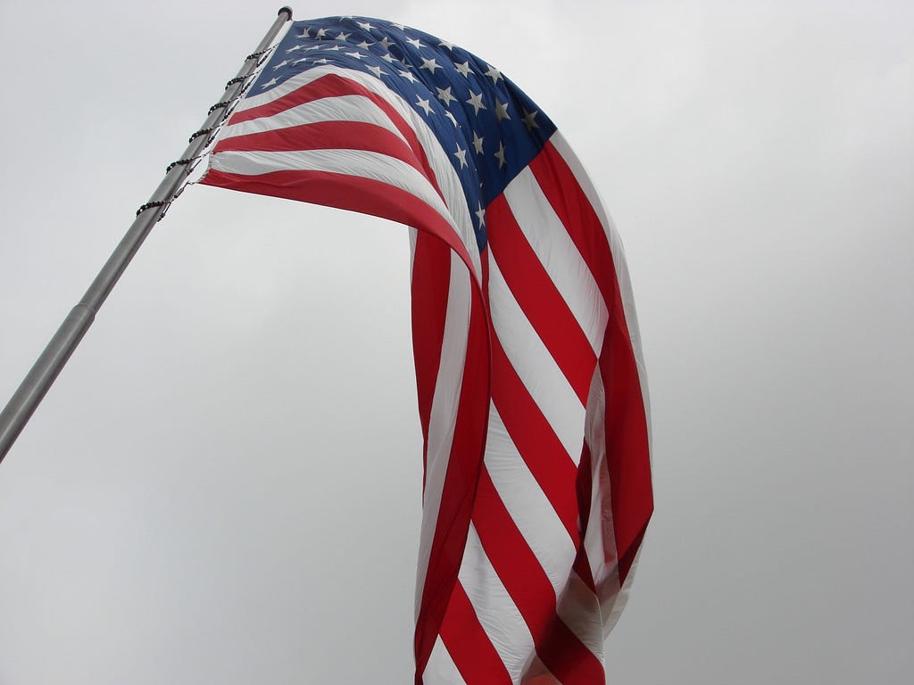 looking up at a USA flag on a flag pole, flying on a cloudy day