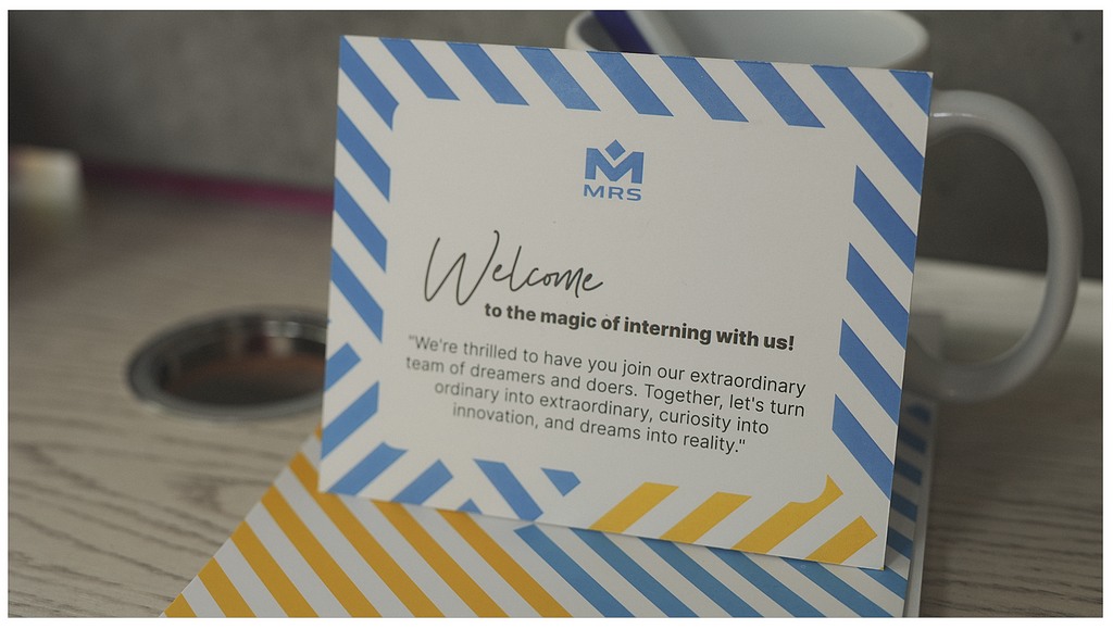 Photo of a card with a Welcome Note in front of a mug. A notebook can be seen underneath the card. | MRS Internship Program 2023