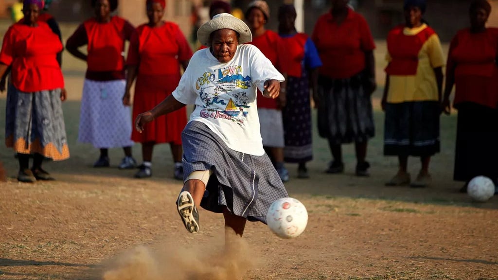 A woman kicking a ball on a dirt field.