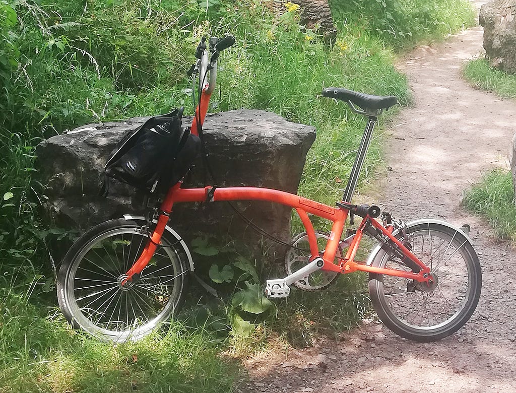 An orange folding bike propped against a large rock.