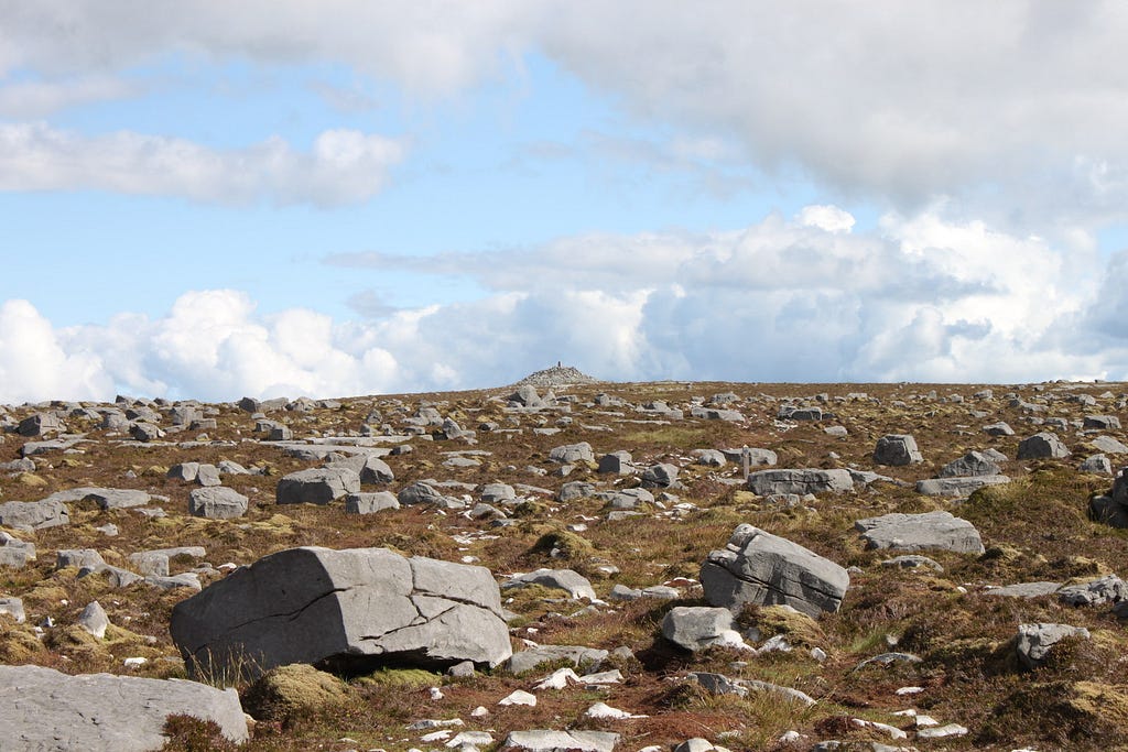 Cuilcagh Mountains. A brown grassland strewn with rectangular boulders and some sort of shrine in the distance.