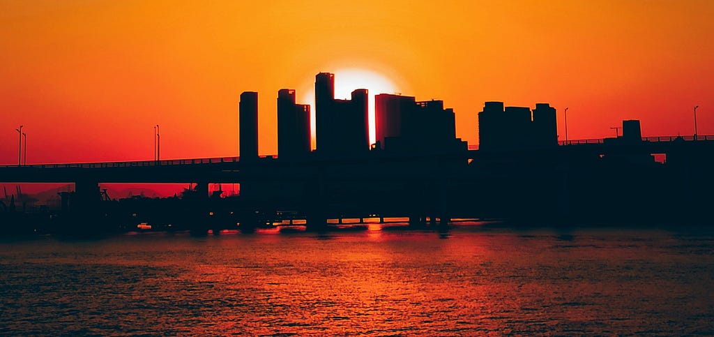 Photo of an orange sky and sun setting on a city downtown skyline.