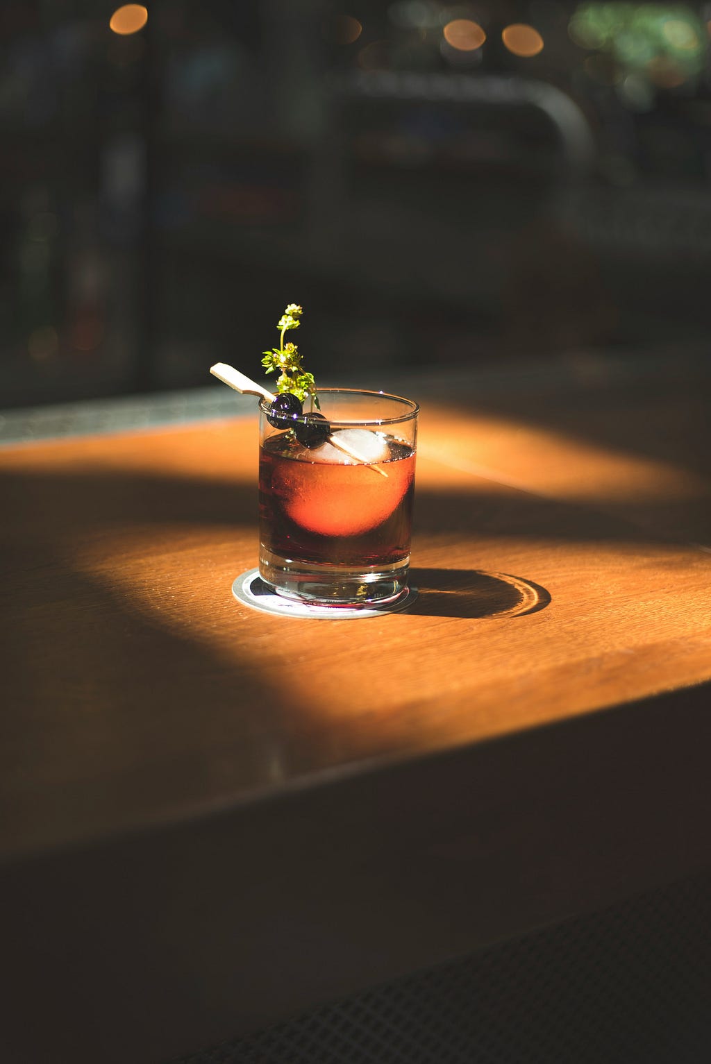 a glass with brown liquor garnished with cherries and a sprig of an herb