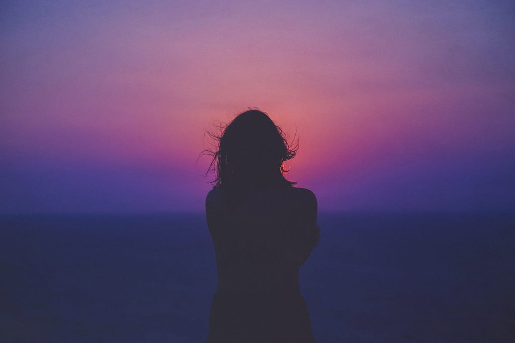The silhouette of a woman is seen against the backdrop of a dark, purple and pink sunset.