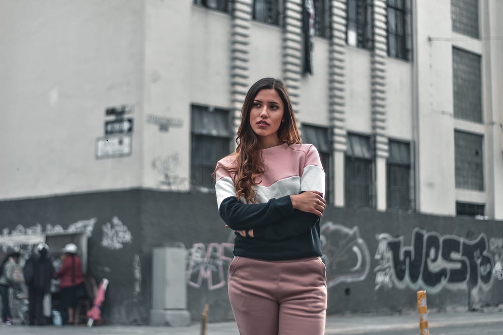 Money mindset: Woman in city with arms crossed looking grumpy