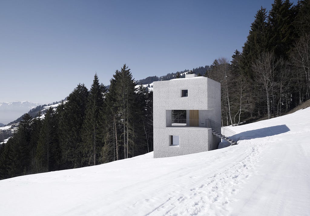A single concrete structure sits on a mountainside, surrounded by snow.