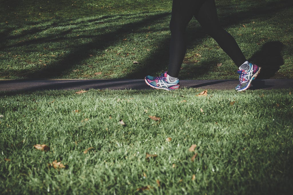 On a path between grass, a person in running shoes and leggings is walking.