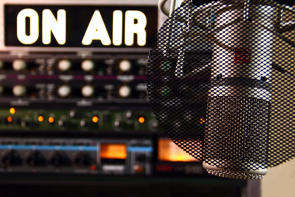 The words “on air” are displayed in the backdrop of a radio studio behind a microphone.