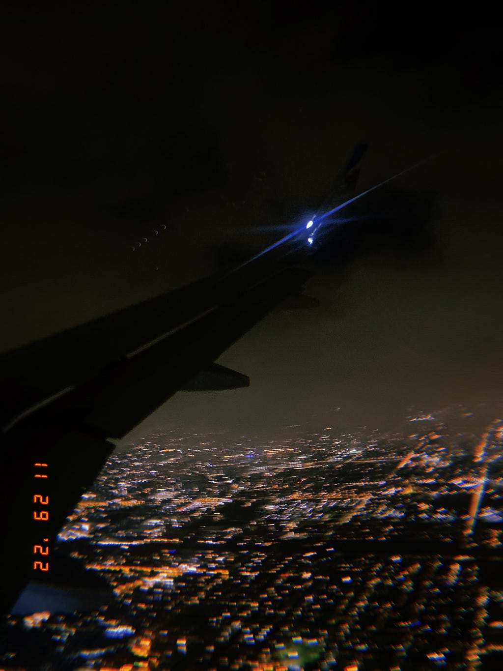 an image of a plane’s right wing drapped in shadows against a city lights at night