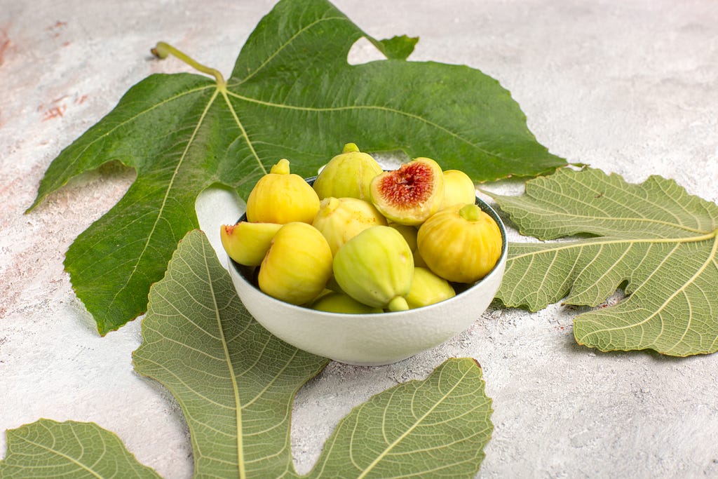 Fig fruit in a bowl surrounded by fig leaves