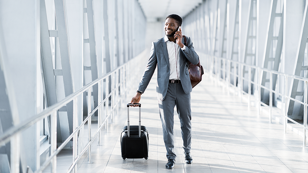 Businessman talking on cell phone while walking through airport with roller bag.