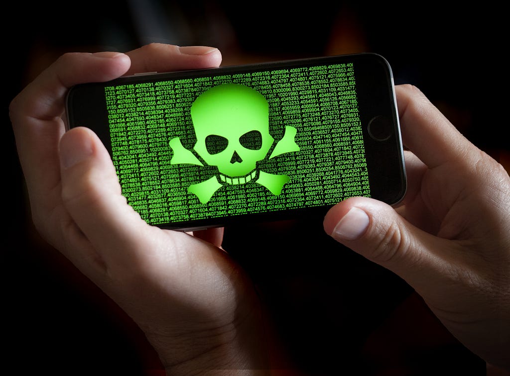 A smartphone held in hands showing a green colored skull and bones symbol.