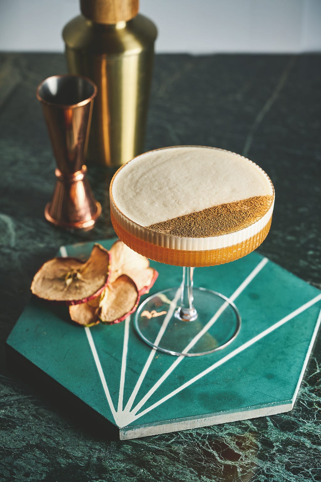 a cocktail with foam and cinnamon on top sitting on a marble tabletop