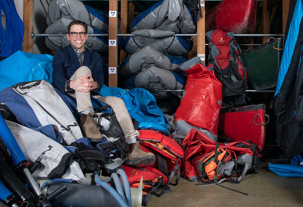 A picture of Will Rice sitting among piles of camping gear.