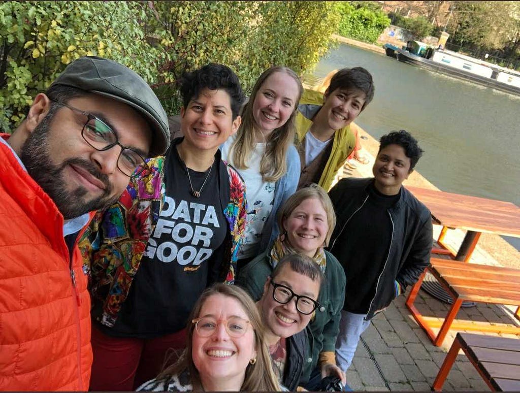 A selfie of the eight people that made up the DataKind team in early 2022, smiling, outside together next to a canal in the sunshine