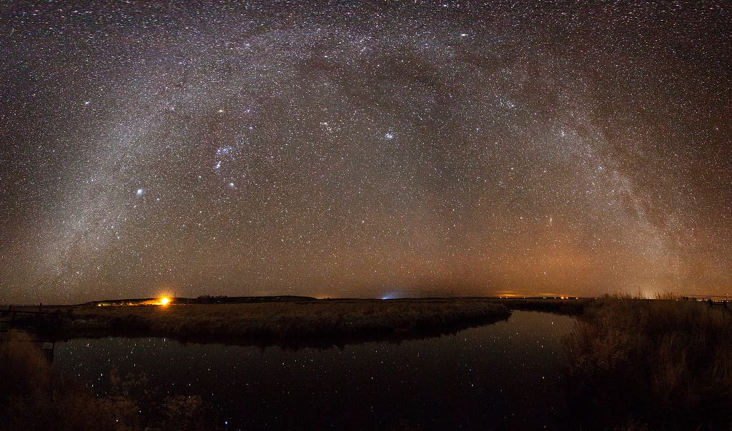 The Milky Way arcs in a half circle over the bend in a river, with stars reflecting.